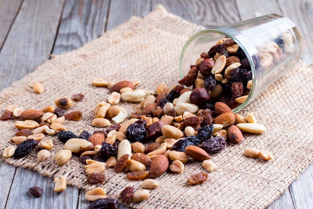 A cup with trail mix spilling out onto a burlap cloth