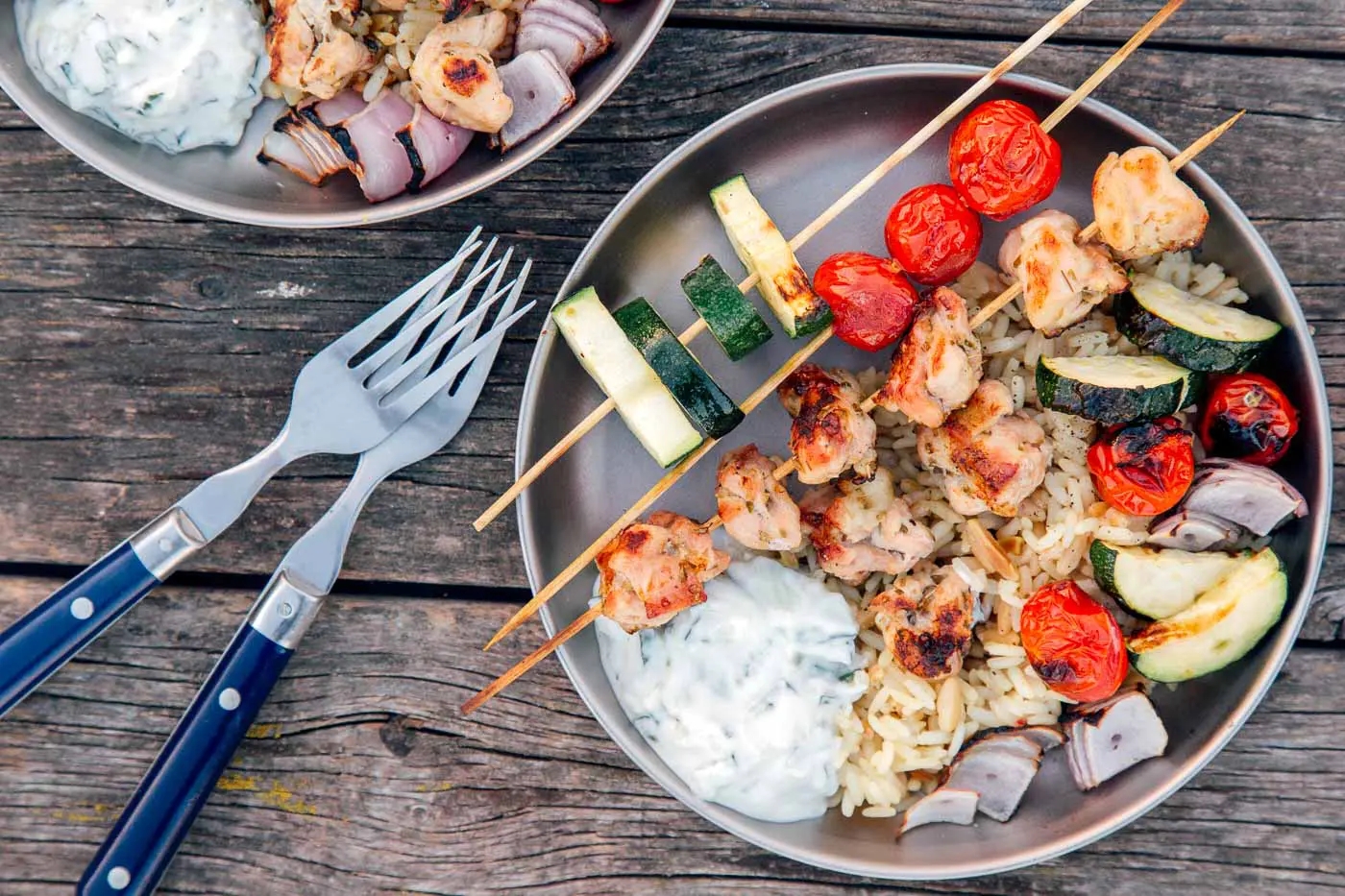 Plates with kabobs, rice, and veggies on a table, all setup for camping meals